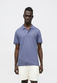 Soe sinine polo särk kraega, ees kolm nuppu ja väike kollane logo vasakul rinnal; kombineeritud valgete tekstuursete lühikestega.