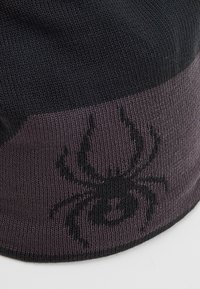 Berretto lavorato a maglia in nero e grigio scuro con una grafica di un ragno nero prominente. Texture morbida e forma aderente per calore e comfort.
