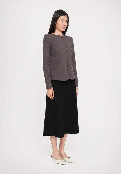 Gray textured long-sleeve top with a round neckline, paired with a black knee-length skirt and white mules. Simple, streamlined design.