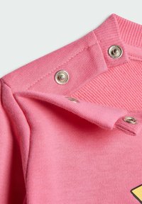 Tejido rosa con un cuello acanalado texturizado, que presenta cierres de presión plateados. El material parece suave y ligero, adecuado para el uso casual.