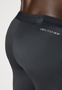 Schwarze Dri-FIT ADV Leggings mit gerippter Textur, hohem Bund und Logo auf der Rückseite, entworfen für optimalen Komfort und Unterstützung.