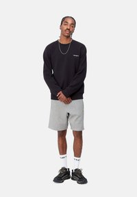 Black sweatshirt, gray shorts, and black sneakers. Notable details include a small logo on the sweatshirt and patterned laces on the shoes.