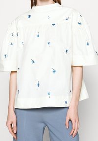 White cotton blouse with short puff sleeves, featuring blue floral embroidery throughout and a round neckline.