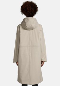 Beige waterdichte jas met een capuchon, lange mouwen en een rechte snit. Kenmerkt zich door minimale stikseldetails en een eenvoudig ontwerp.