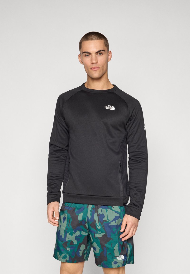 Zwart sportshirt met lange mouwen en raglanmouwen, zachte textuur en een wit logo op de borst, gecombineerd met groene camouflage shorts.