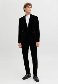 Melnas samta uzvalks ar vienu pogu piegriezumu un šallītes apkakli, apvienots ar šauriem biksēm un spīdīgiem melniem apaviem.