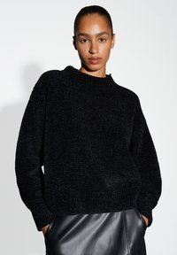 Schwarzer strukturierter Pullover mit hohem Kragen, lockerer Passform und langen Ärmeln, kombiniert mit einem schwarzen Lederrock, der eine glatte Oberfläche zeigt.