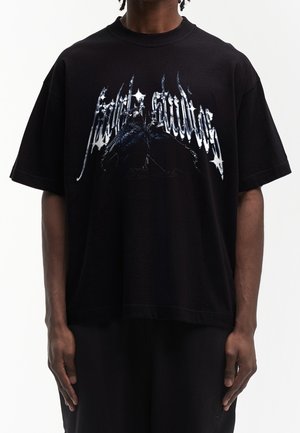 T-shirt noir oversize avec texte gothique métallique et un graphisme détaillé de deux oiseaux noirs face à face sur la poitrine.