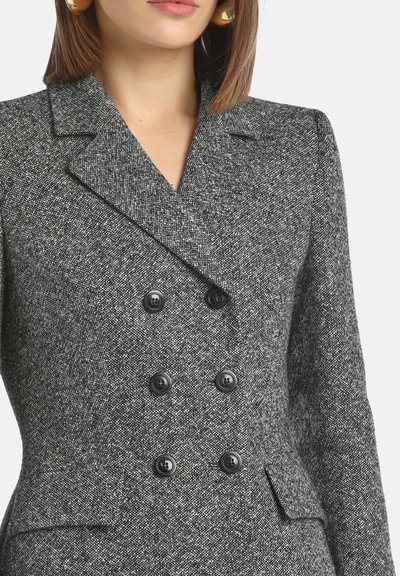 Blazer double boutonnage en chevrons gris avec revers, boutons noirs et poches frontales, doté d'un tissu texturé.