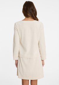 Beige geripptes Langarmkleid mit geradem Schnitt, das einen runden Halsausschnitt und ein gestuftes Rockdesign am Saum aufweist.