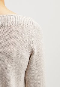 Strickpullover in hellbeige mit strukturierter Oberfläche. Verfügt über einen gerippten Kragen und glatte Ärmel, die ein minimalistisches Design hervorheben.