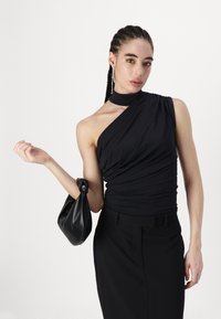 Haut noir à une épaule en tissu doux avec une texture froncée. Associé à une jupe noire moulante taille haute et un sac à main noué.