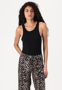 Svart ribbet singlet med brede stropper, paret med leopardmønstrede vide bukser med høy midje og knappelukking.