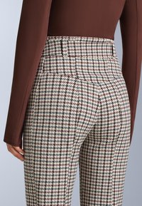 Kockované nohavice s vysokým pásom v krémovej, čiernej a burgundskej farbe; hladká tkanina s vzorom houndstooth a upravené zadné vrecká.