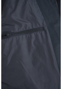 Giacca blu navy con una texture liscia, dotata di una tasca con zip e pannelli a contrasto, progettata per funzionalità e calore.