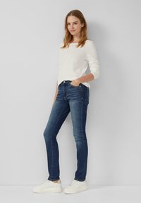 Jean skinny en denim bleu foncé, avec une taille mi-haute et un design classique à cinq poches. Associé à un haut léger à manches longues et des baskets blanches.