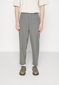 Szare spodnie w paski o zwężającym się kroju, wykonane z lekkiego materiału. Noszone z beżową bluzką i szarymi butami, prezentujące swobodny wygląd.