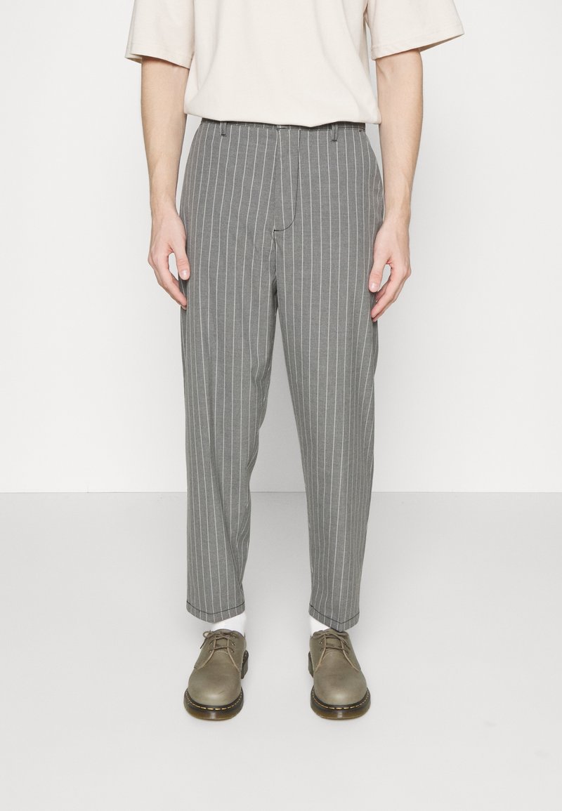 Szare spodnie w paski o zwężającym się kroju, wykonane z lekkiego materiału. Noszone z beżową bluzką i szarymi butami, prezentujące swobodny wygląd.