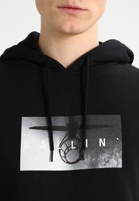 Zwarte hoodie met een voorzijdeafbeelding van een basketbalnet en het woord "BALLIN'" in het wit, gemaakt van katoen met een gladde textuur.