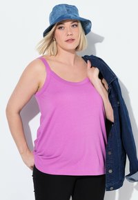 Top con scollo tondo rosa, dal taglio morbido e realizzato in materiale soffice. Abbinato a una giacca di denim e un cappello a secchiello blu. Pantaloni neri completano l'outfit.