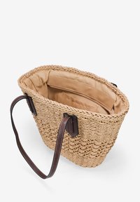Bolso tote de paja trenzada con asas de cuero marrón, con un suave forro beige y bolsillos interiores para organización. Diseño de apertura superior.