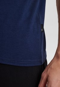 Navy blue cotton t-shirt with a smooth texture, side vent detail, and small black branding tag on the hem.