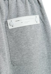 Los joggers de algodón gris cuentan con un parche de cuero blanco en el bolsillo trasero, texto en relieve y dos botones visibles para un detalle adicional.