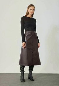 Jupe midi en cuir marron avec une coupe évasée, dotée d'une fermeture à boutons à l'avant. Associée à un haut ajusté noir à manches longues et à des bottes à talons noires.