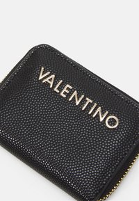 Portefeuille en cuir noir avec finition texturée, featuring le logo doré "VALENTINO". Fermeture zippée avec détails en métal doré. Forme rectangulaire.