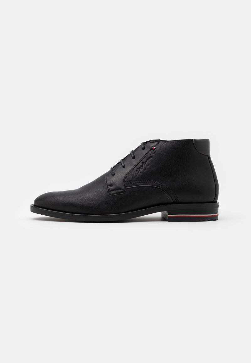 Bottine noire en cuir avec laçage, petit talon et logo discret de la marque sur le côté, sur fond blanc uni.