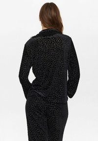 Must mustri mustukate loungewear komplekt, mis sisaldab tekstuuriga täppidega kangast, pikad varrukad ja mugav lõige. Kangas on pehme ja luksuslik.