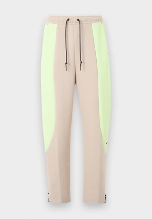 Béžové teplákové nohavice so svetlozelenými bočnými panelmi, čiernym sťahovacím pásom, zúženými nohavicami a malým čiernym logom pri ľavom členku.