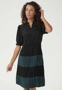 Čierne šaty s krátkymi puff rukávmi, prepleteným dizajnom a tromi horizontálnymi farebnými blokmi: čierna a teal. V-krčný strih, elastický pás.