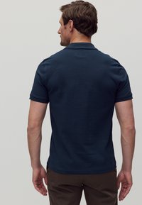 Marineblå polo med klassisk krage, korta ärmar och en mjuk textur, med en sidslitskjol och utan synliga dekorationer.