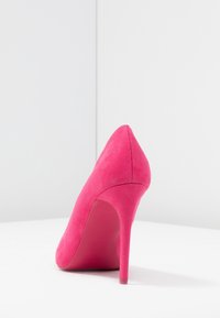 Chaussure à talon haute en suède rose vif avec un bout pointu et un talon aiguille mince. Texture lisse et design minimaliste.