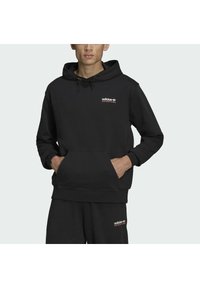 Juodas medvilnės džemperis su kapišonu, turi kengūrų tipo kišenę, reguliuojamą raištelį ir raudoną "adidas ADVENTURE" logotipą krūtinėje.