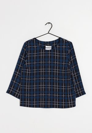 Haut à manches 3/4 en tartan bleu et noir, fabriqué en tissu doux, avec un col rond et des fentes sur les côtés pour faciliter les mouvements.