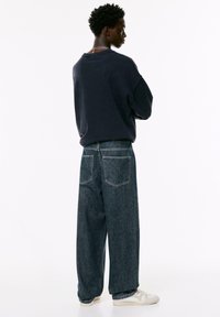 Hanorac de mari dimensiuni, de culoare bleumarin, cu umeri căzuți, asortat cu blugi de denim de talie medie, cu croială largă și buzunare la spate. Adidași casual.