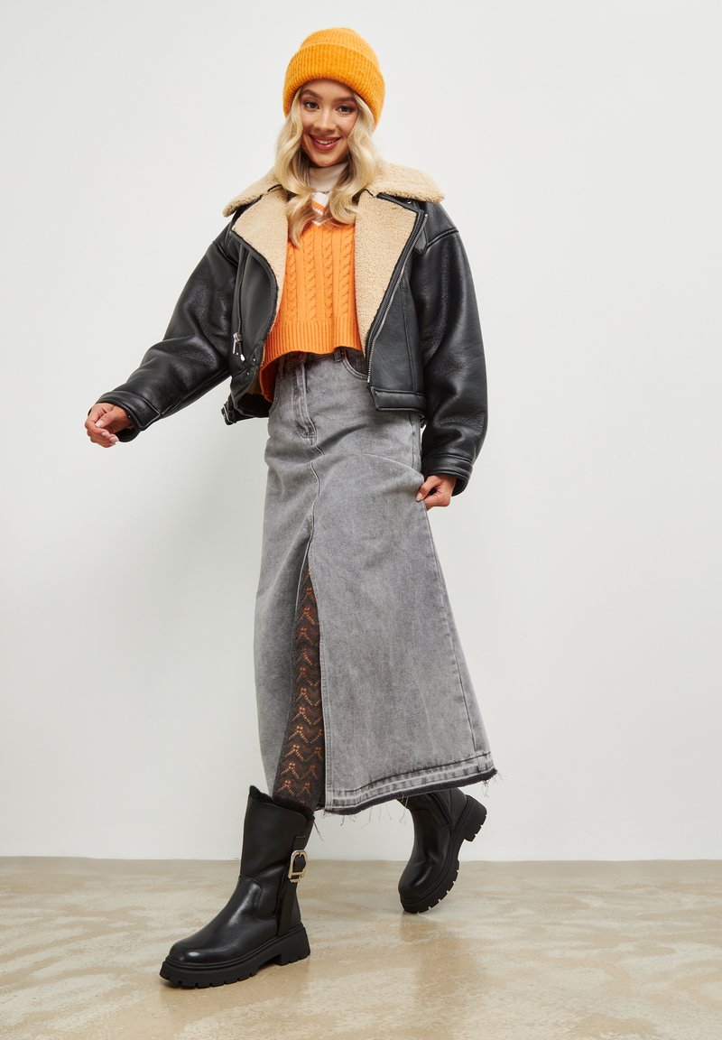 Svart läderjacka med beige shearlingkrage, orange stickad tröja, grå denimkjol med sidofrånskärning och svarta ankelboots.