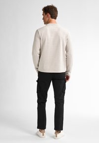 Suéter gris claro texturizado con cuello redondo, combinado con pantalones cargo negros que tienen bolsillos laterales y zapatillas beige.