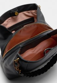 Melna teksturēta ādas soma ar plašu interjers, gaismas persiku oderi, zelta rāvējslēdzis un savītā melna rokturis.