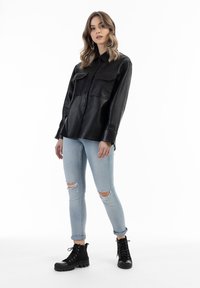 Sort læder skjorte med knapper og to brystlommer, parret med lys blå slidte skinny jeans og sorte snørebånd ankelstøvler.
