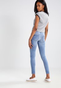 Top de manga corta a rayas blancas y negras, combinado con jeans ajustados de color azul claro y zapatillas blancas sin cordones, con un diseño ajustado y detalles sencillos.