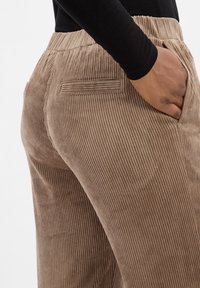 Jasnobrązowe spodnie w kord sztruks, z pionowym prążkowaniem, bocznymi kieszeniami i elastycznym pasem dla wygody.