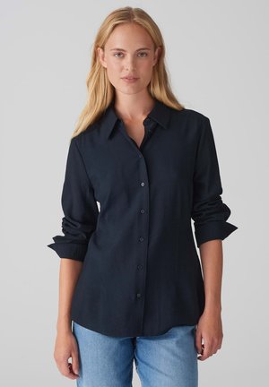 Navy button-up shirt in lightweight fabric, featuring a classic collar, long sleeves with rolled cuffs, and a curved hemline.