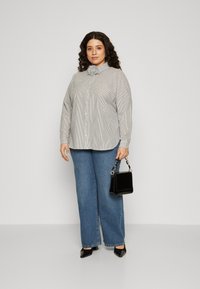 Light gray striped shirt with a bow tie collar, paired with wide-leg blue denim jeans. The model holds a small black handbag and wears black heels.