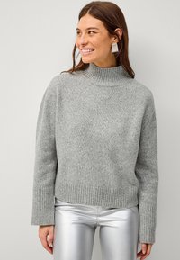 Maglione grigio a collo alto lavorato a maglia con orlo e polsini a coste, caratterizzato da una vestibilità morbida. Abbinato a pantaloni argentati lucidi.
