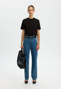 Juodas medvilninis marškinėliai, mėlynos aukšto liemens džinsai, juodas diržas, juodas rankinukas, smailaus nosies juodi bateliai, minimalistinis dizainas, neutralus fonas.