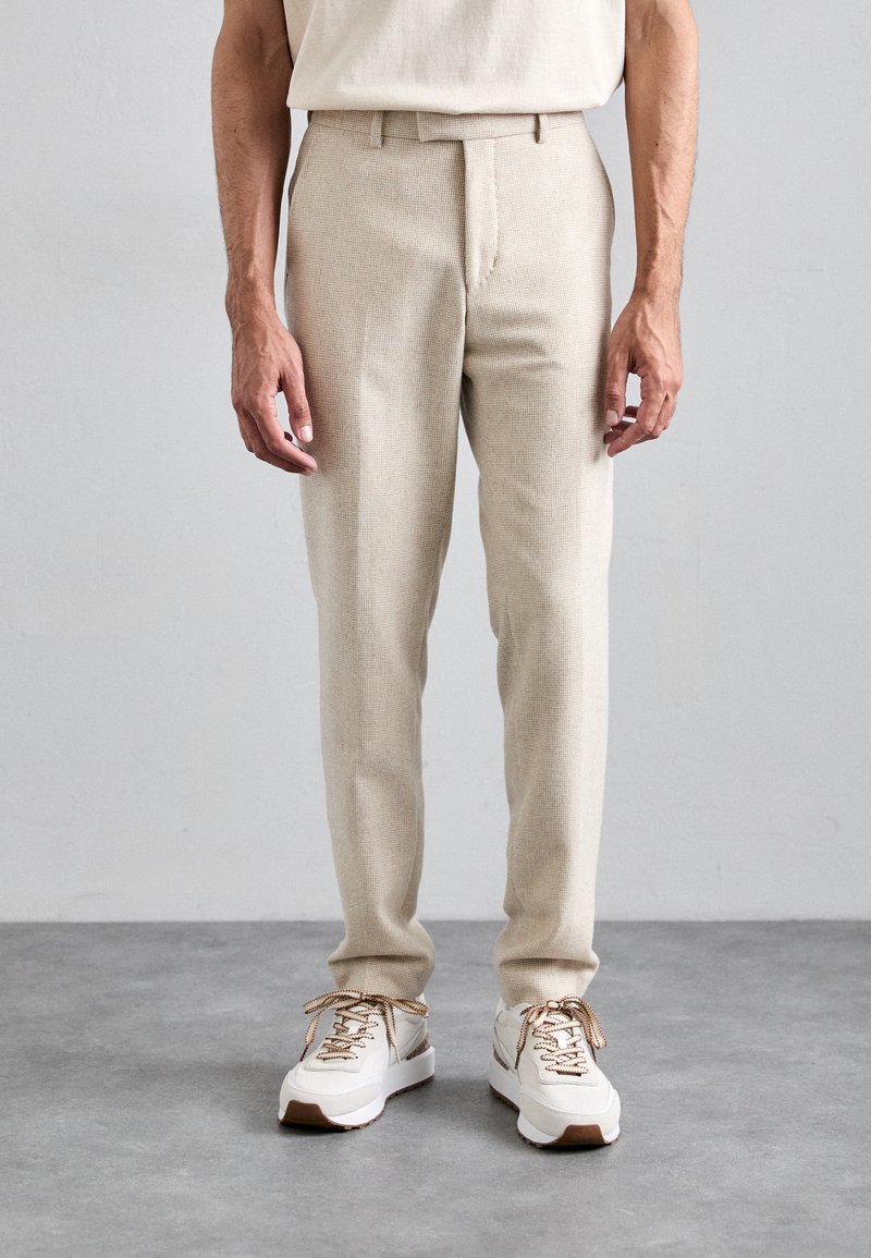 Beige wool blend trousers with a textured pattern, slim fit, mid-rise waist, and front crease, paired with white athletic shoes.
