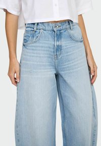 Heledad sinine, kõrge vöökoht ning laiad jalad, millel on pleekinud viimistlus, nähtavad õmblused ja kerge kulumine kangal. Tavalised ees taskud.